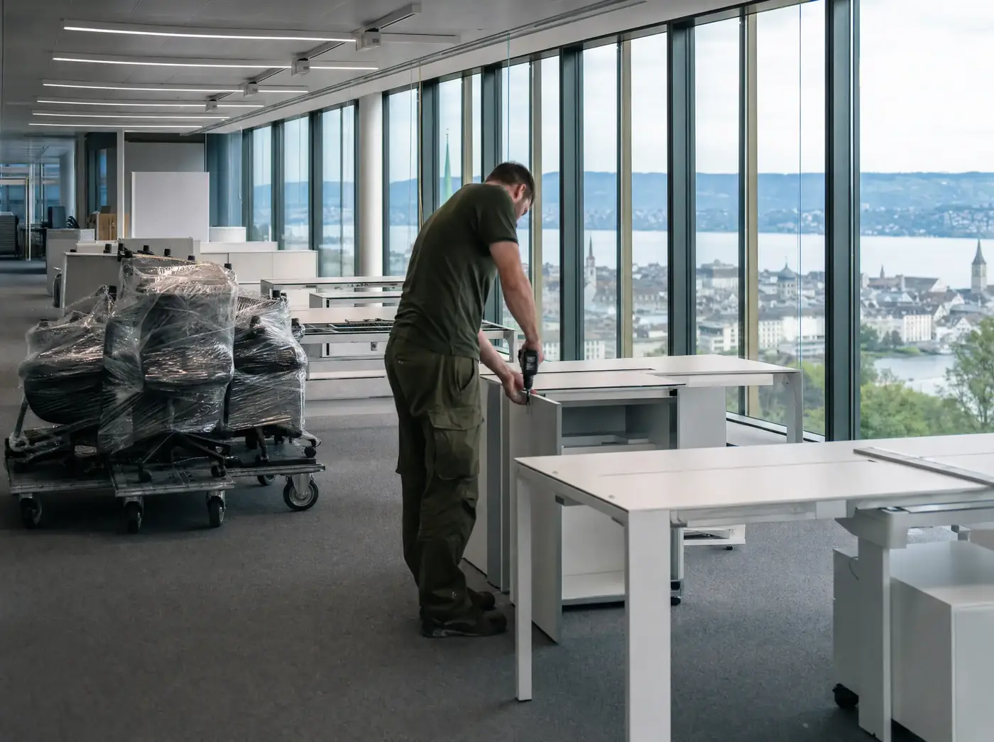 Moderner Büroraum während einer Betriebsauflösung, ein Mitarbeiter demontiert einen Schreibtisch